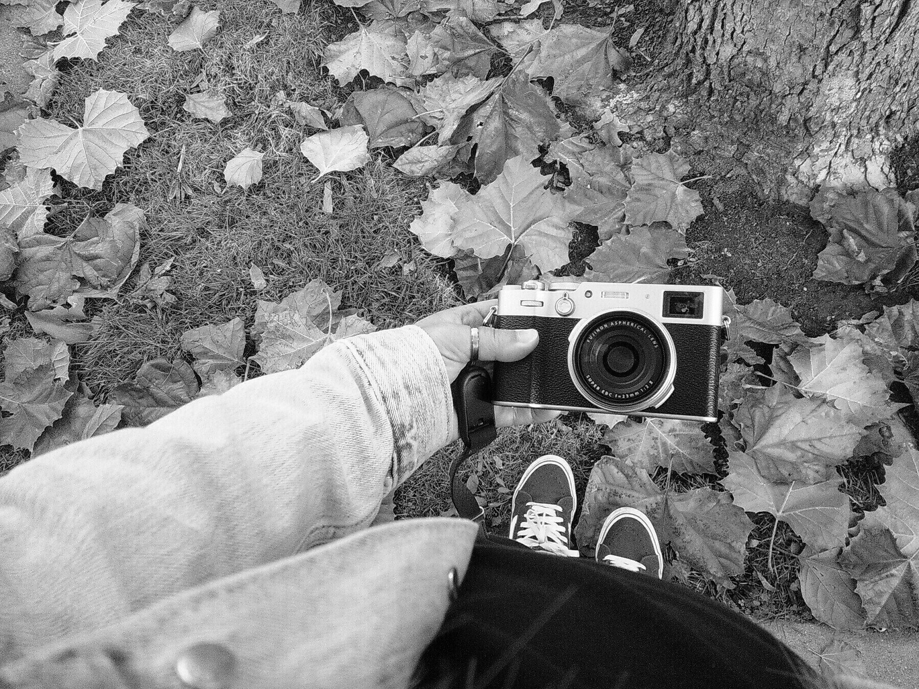 black and white photo. hand holding a camera shot from above, with shoes and leaves visible on the ground