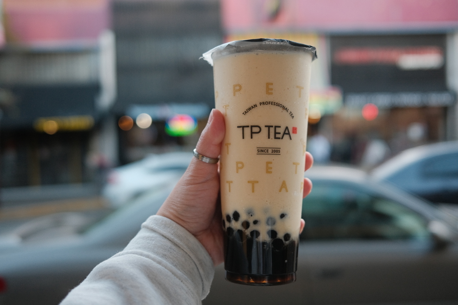 A hand holding a bubble tea. The cup says TP tea and there are tapioca pearls at the bottom of a brown drink.