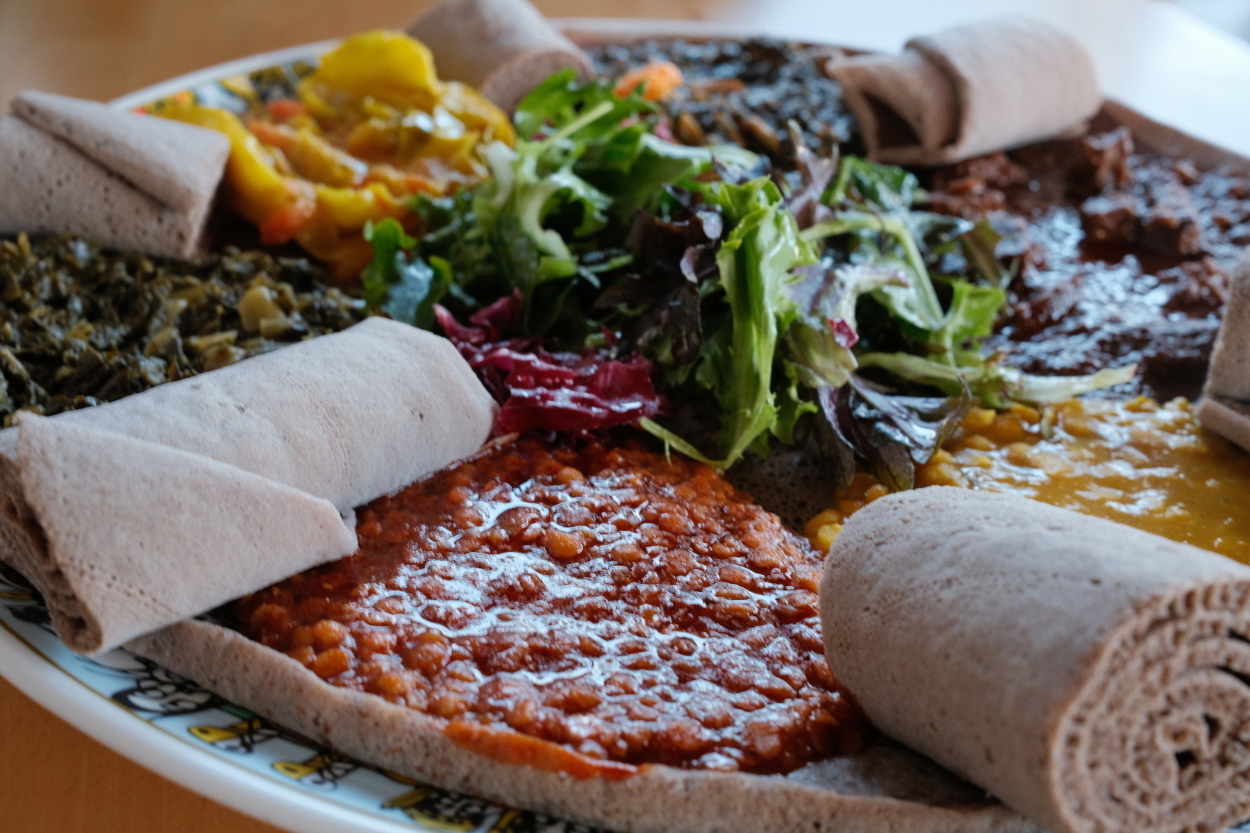 Plate of Ethiopian cuisine with injera bread rolls, lentils, cooked greens, and salad.